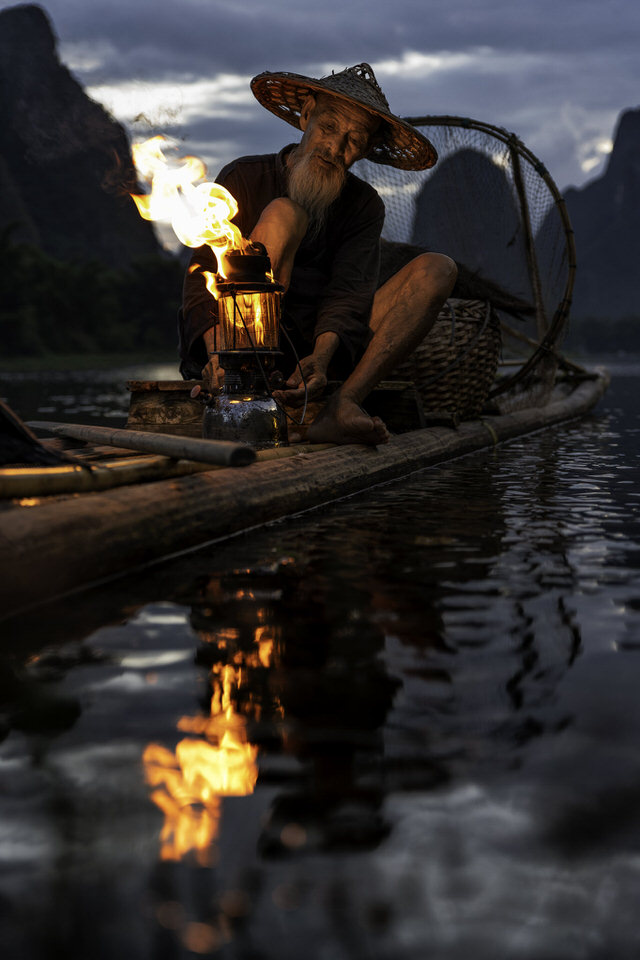 A cormorant fisherman lighting his lantern on a bamboo raft in Guilin at sunset.