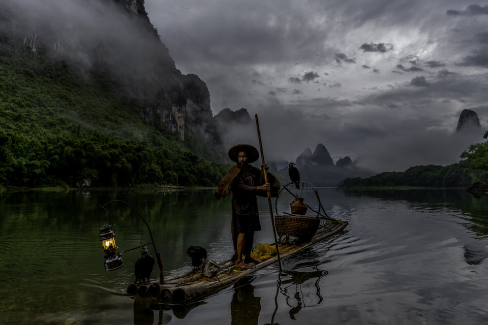 A cormorant fisherman with his bird at sunrise on the Li River in Guilin, China.