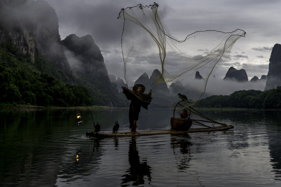 Cormorant fisherman casting his fishing net at sunrise on the Li River in Guilin, China.