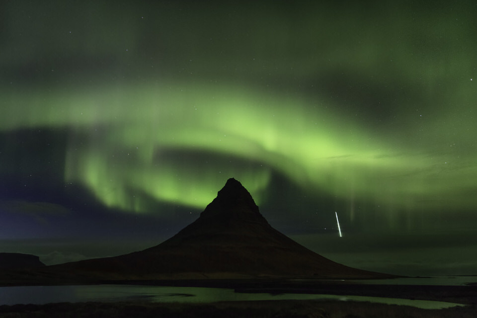 Northern Lights over a mountain in Iceland with a shooting star in the night sky